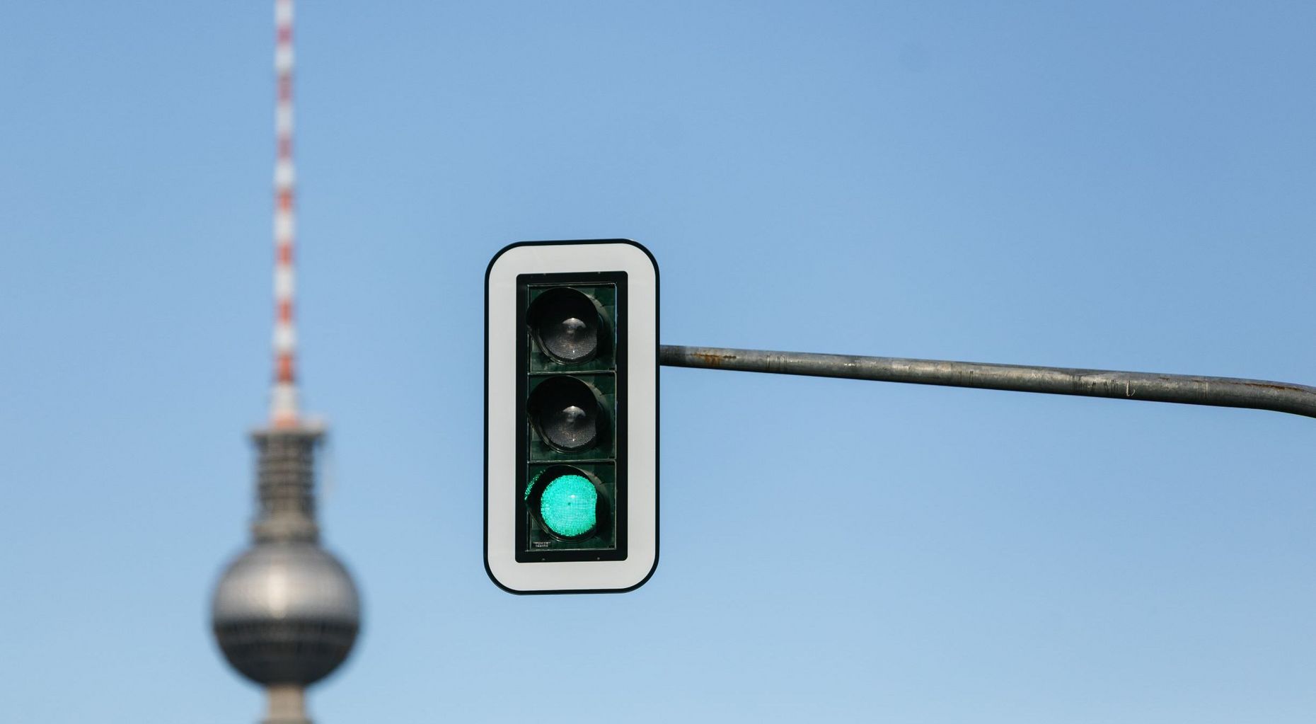 Grüner Signalgeber vor blauem Himmel und im Hintergrund die Spitze des Berliner Fernsehturms