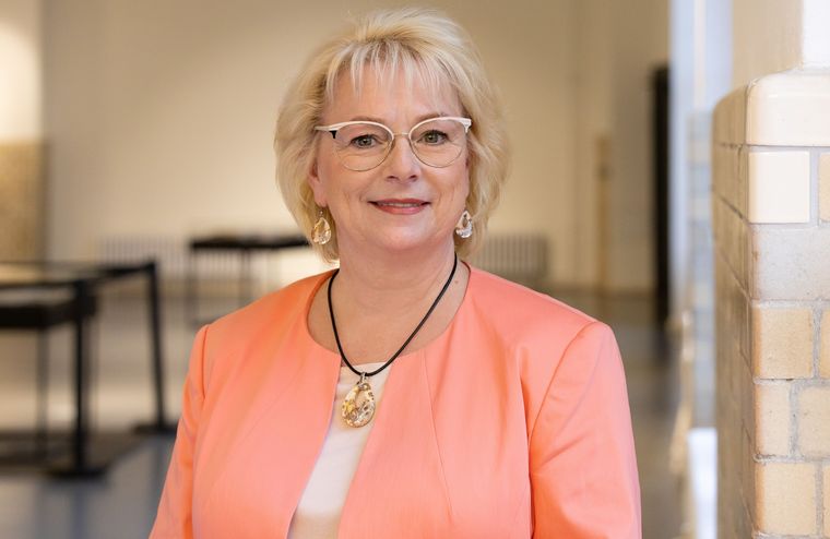 infraSignal-Geschäftsführerin Katharina Marienhagen steht in einem lachsfarbenen Sakko vor einer gefliesten Wand