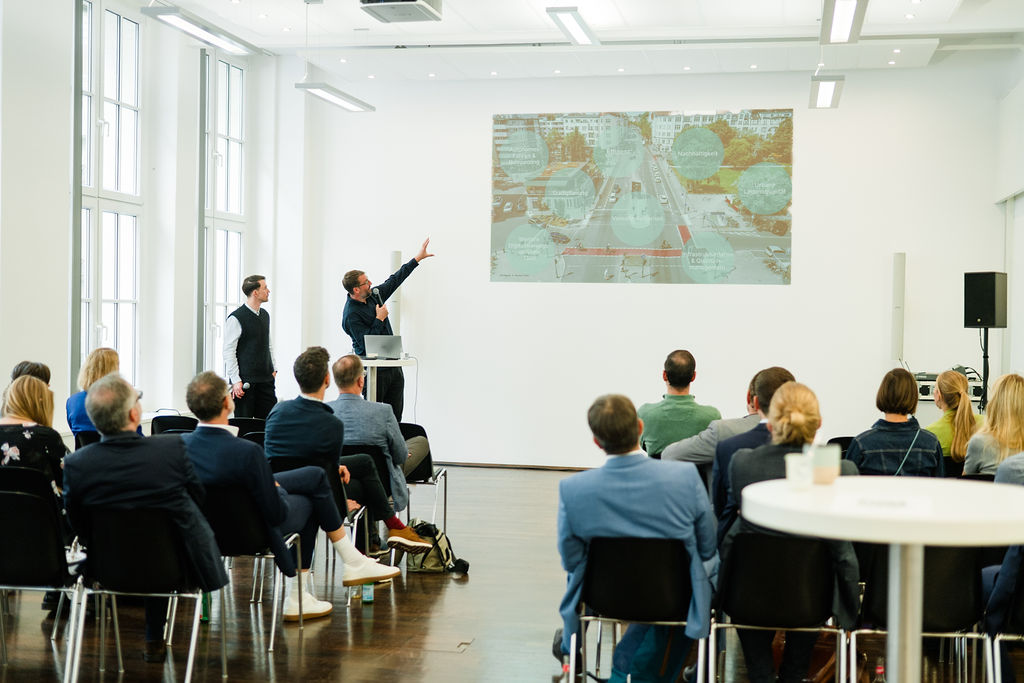 Workshop-Situation: Zwei Redner stehen vorne und erklären dem Publikum die Präsentationsfolie 